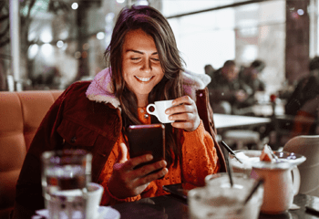 woman drinking coffee in cafe while scrolling on phone